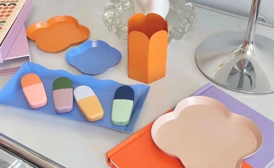 Cute stationery items, including colorful trays and erasers, displayed on a white desk with a reflective lamp.