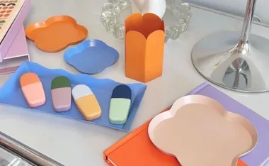 Cute stationery items, including colorful trays and erasers, displayed on a white desk with a reflective lamp.