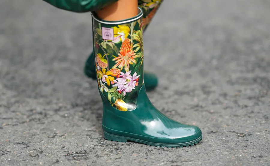 Green gumboots with colorful floral designs, worn on a textured grey surface.