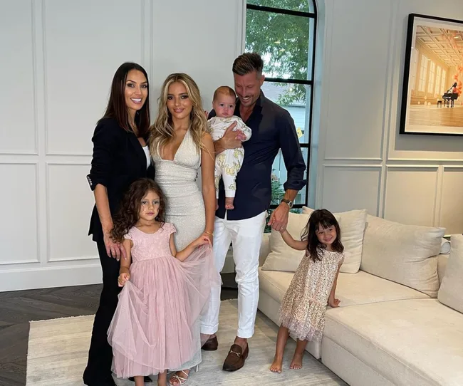 A family of six posing in a stylish living room, including three young children and a baby.