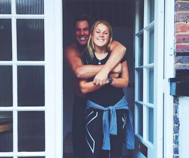 Father hugging daughter, both smiling, standing in a doorway.