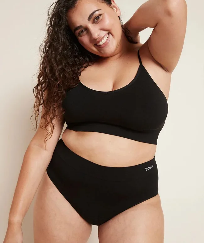 Smiling woman in black underwear poses confidently with hand behind her head.