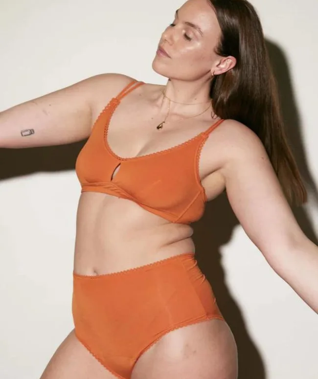 Woman in orange lingerie set posing against a neutral background.