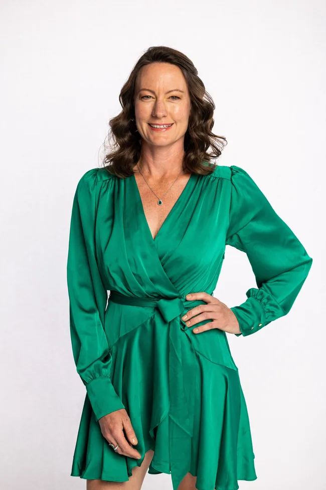 Woman in a green dress smiling with hand on hip against a white background.