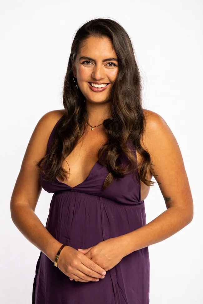 A woman in a purple dress smiling with long dark hair against a white background.