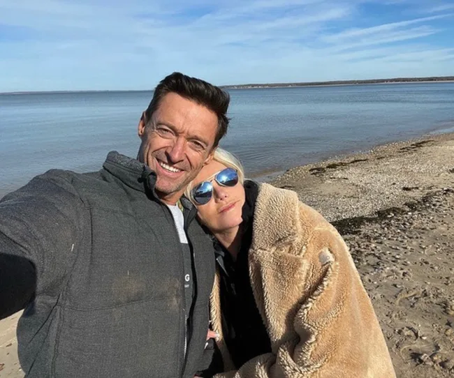 Two people taking a selfie on a beach, with the ocean and clear sky in the background.