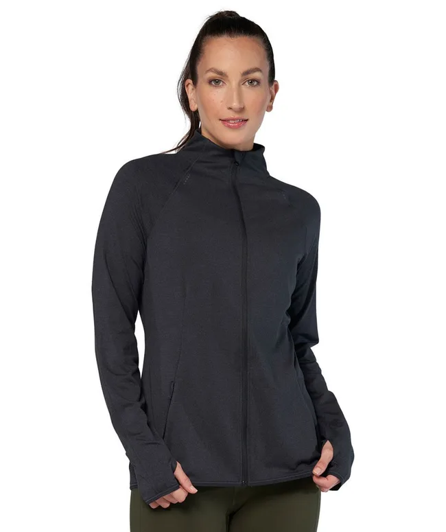 A woman in a black zip-up jacket with her hands in the pockets, against a white background.