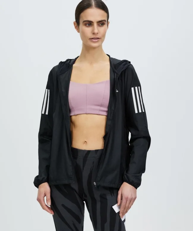 A woman in a pink sports bra, black athletic jacket, and patterned leggings, standing in a neutral pose.