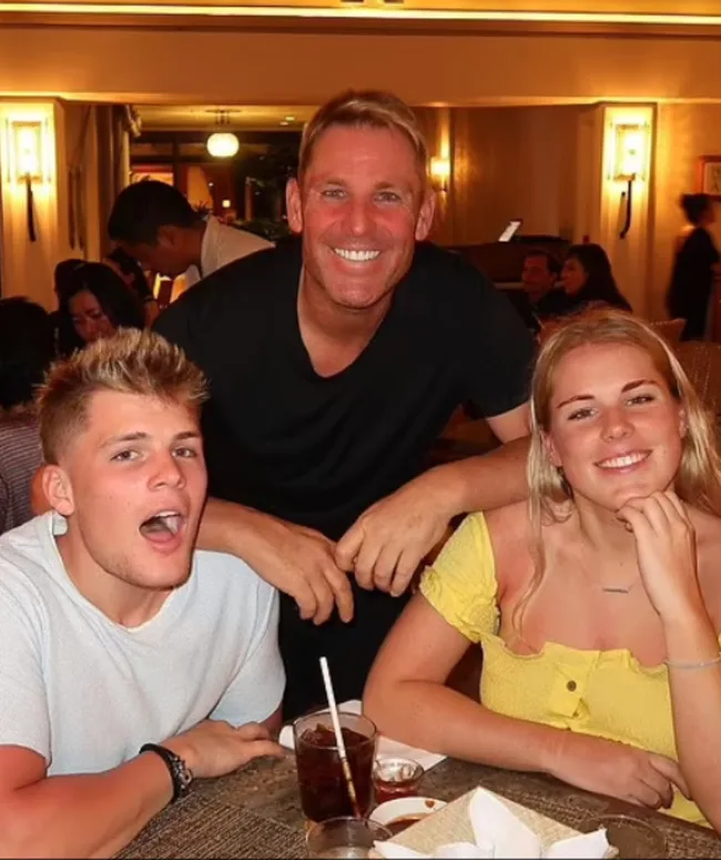 Three people smiling at a dining table in a warmly lit restaurant setting.