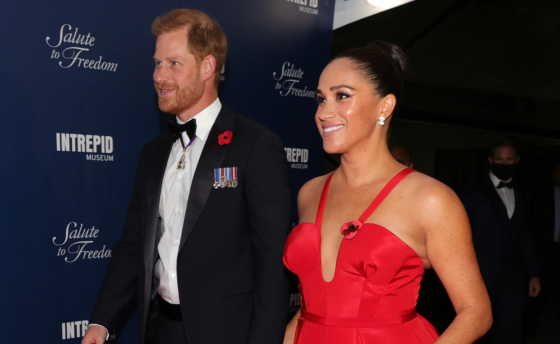 A man in a tuxedo and a woman in a red dress smile, attending an event at the Intrepid Museum.