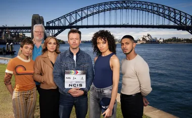 Cast of "NCIS: Sydney" at Sydney Harbour, with the Sydney Opera House and Bridge in the background, holding a clapperboard.