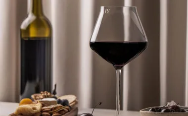 A personalized wine glass with initials "JY," a bottle, and a charcuterie board on a table.