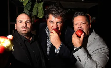 Three judges holding and biting apples, looking directly at the camera with dramatic expressions.