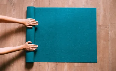 Person's hands rolling a teal Pilates mat on a wooden floor.