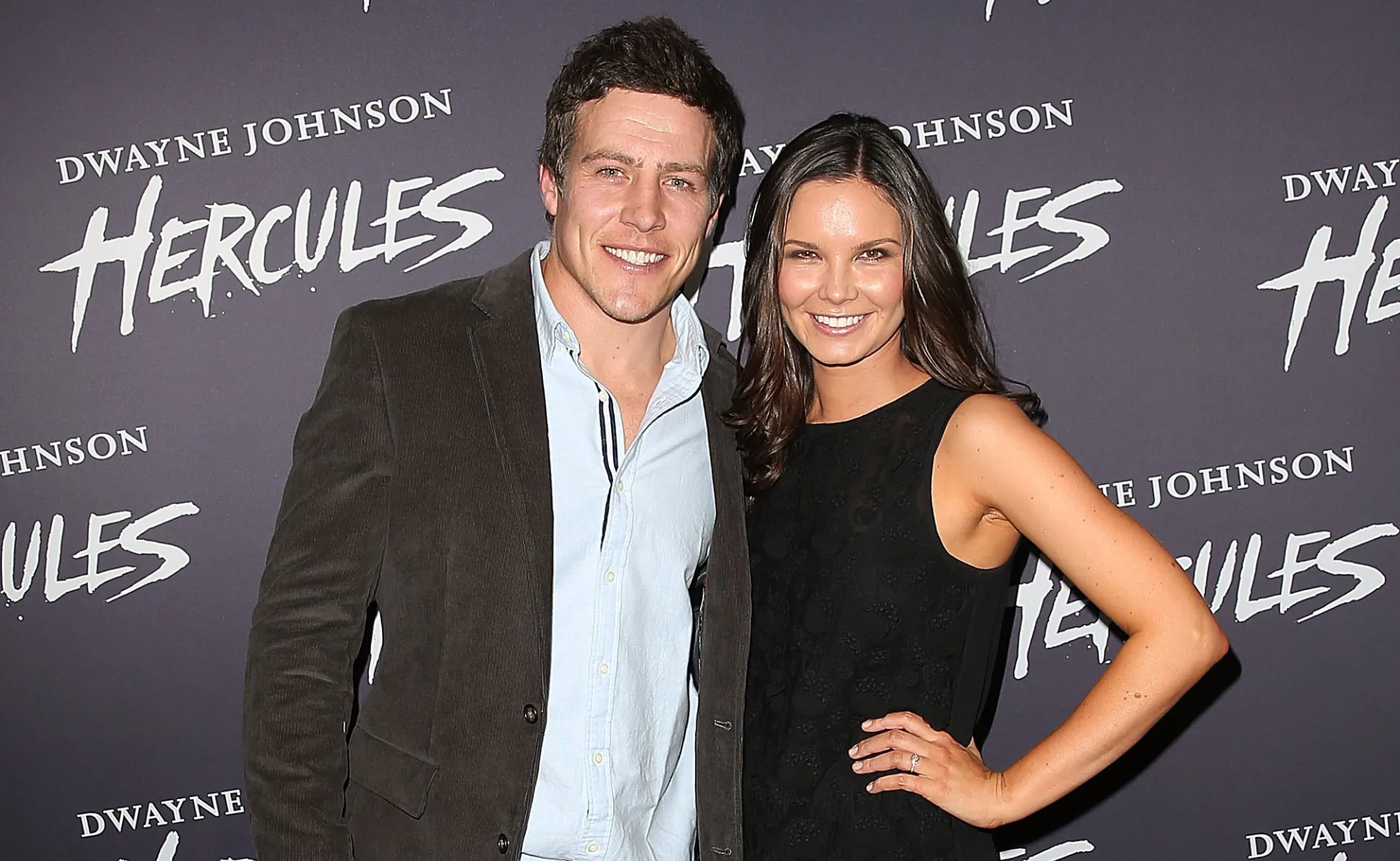 Couple posing at "Hercules" event with Dwayne Johnson signage in the background.
