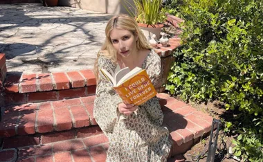Woman in floral dress reading "I Could Live Here Forever" by Hanna Halperin while sitting on brick steps outdoors.