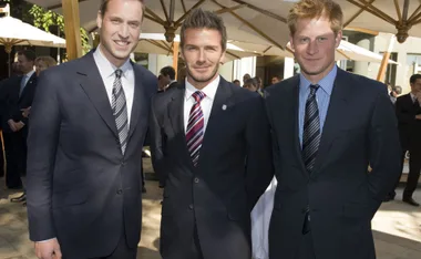 Three men in suits smiling at an outdoor event with guests in the background.