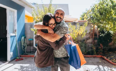 Father and daughter hugging happily outdoors, holding gift bags.