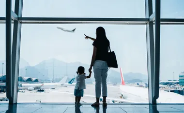 Mother and child at airport window, pointing at a plane taking off.