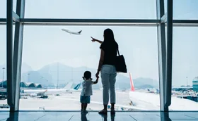 Mother and child at airport window, pointing at a plane taking off.