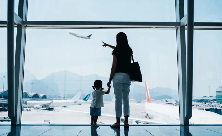Mother and child at airport window, pointing at a plane taking off.