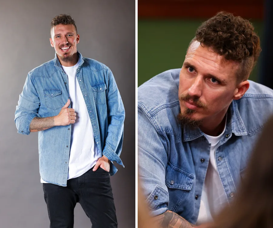 A man in a denim shirt poses and looks thoughtful, with short curly hair and a goatee.