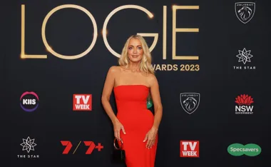 Blonde woman in a red dress at the Logies 2023 event, standing in front of the event backdrop.