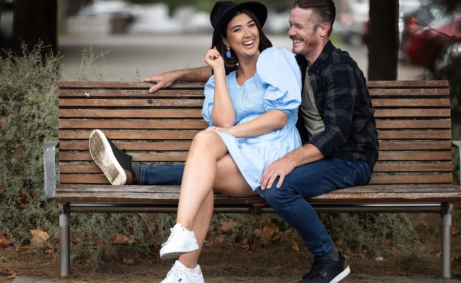 A couple sitting on a park bench, smiling and laughing together.