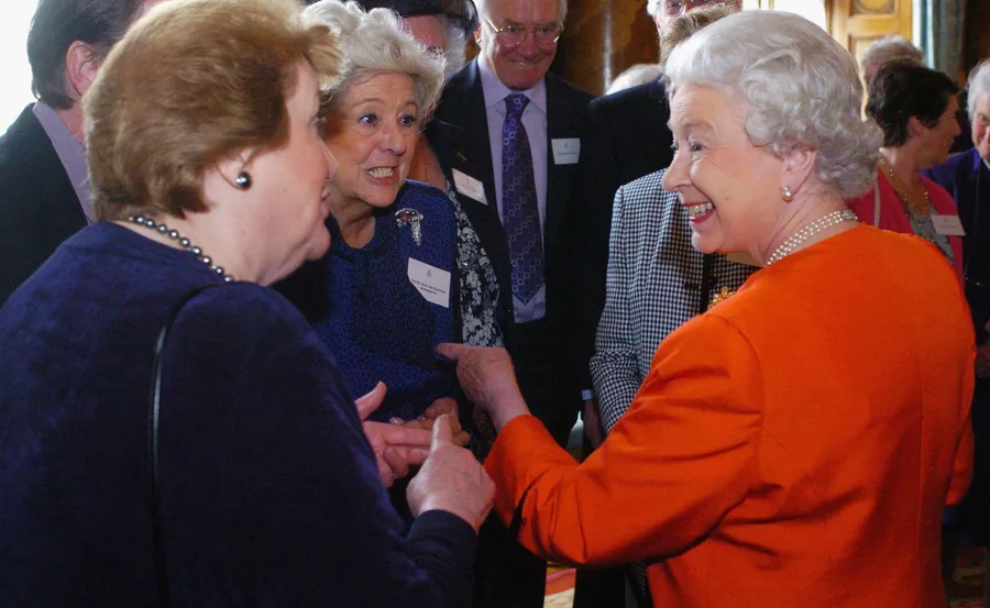 Women smiling and conversing in a group setting; one in an orange outfit appears engaged and happy.
