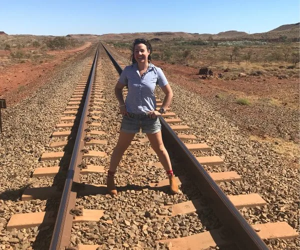 Person standing confidently on railway tracks in a rural landscape under a clear blue sky.