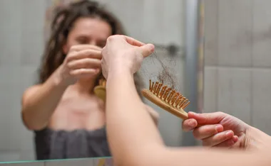 Person holding a hairbrush with hair strands, focusing on hair loss in a bathroom setting.