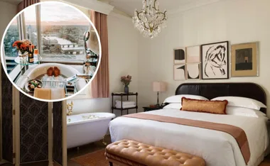Elegant hotel room with a chandelier, large bed, artwork, and a circular inset showing a bathtub with a city view.
