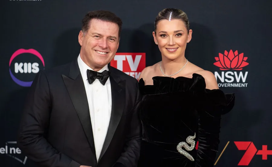 A couple in formal attire smiling on the red carpet, with event logos in the background.