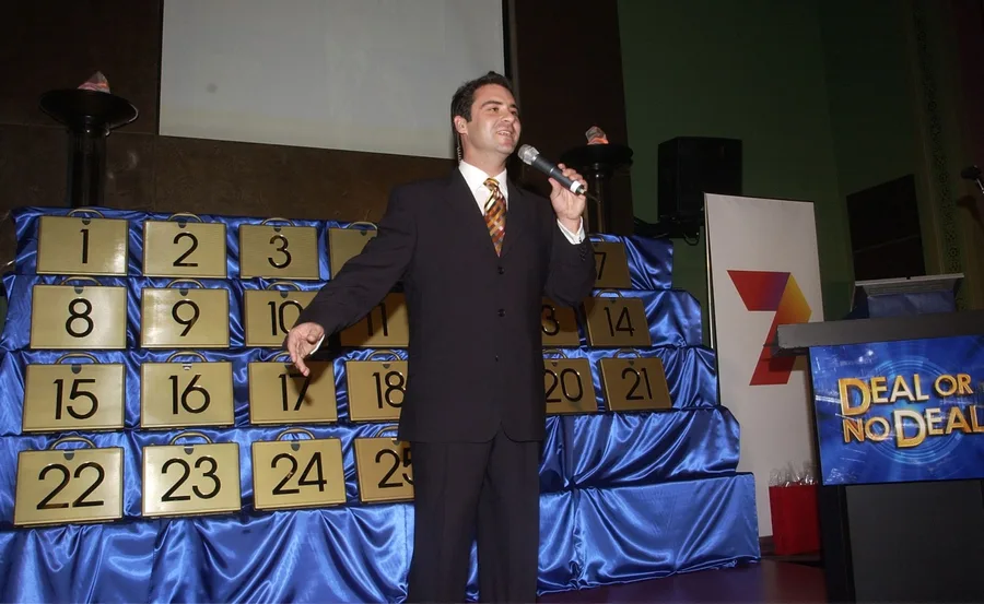 Host on stage with microphone, beside numbered briefcases from "Deal or No Deal."