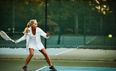Adult woman playing tennis on an outdoor court, preparing to hit a forehand shot.