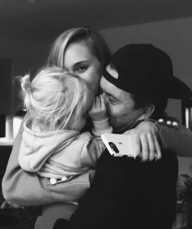 A woman, man, and a child share a close, loving embrace while smiling indoors.