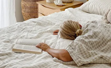 Person lying on a bed with checked linen sheets, a book open nearby.