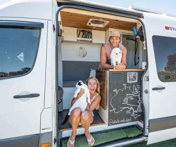 Van life couple with two cats, sitting in the doorway of their camper van, enjoying a sunny day.