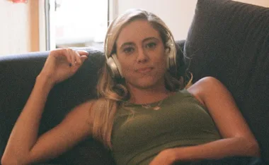 A person wearing headphones, reclining on a couch, looking relaxed with a slight smile.