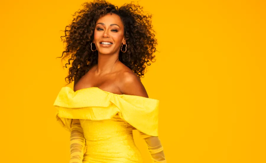 A person in a yellow off-shoulder dress smiles against a vibrant yellow background.
