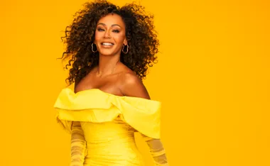 A person in a yellow off-shoulder dress smiles against a vibrant yellow background.