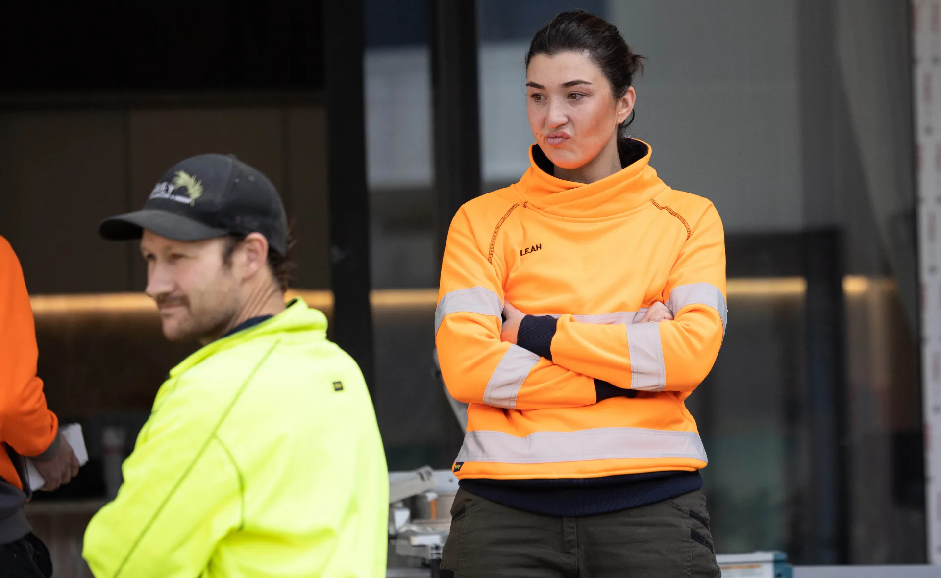 Two people in high-visibility work attire; one looks thoughtful, the other is focused and serious.