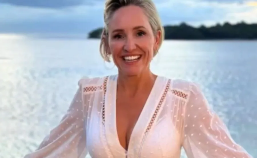 A person in a white dress smiling by the water with a scenic background at sunset.