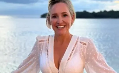 A person in a white dress smiling by the water with a scenic background at sunset.