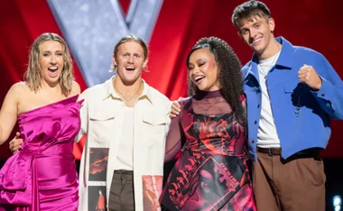 Finalists of The Voice Australia 2023 stand together, smiling on stage with a red and silver backdrop.