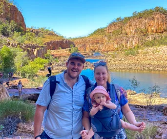 Family of three posing in front of a scenic rocky landscape with a river, wearing casual hiking attire.