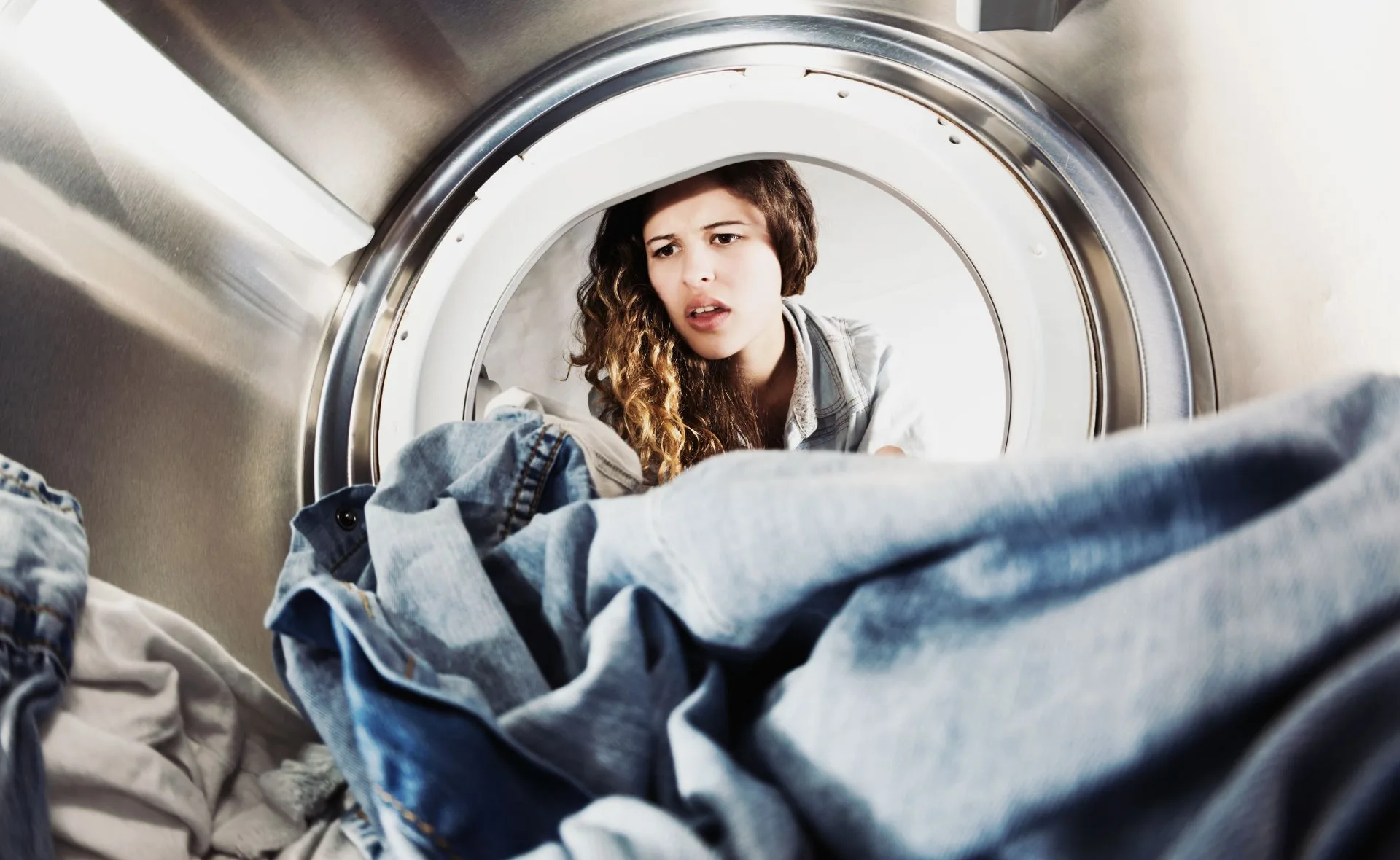 Woman looking into a washing machine, appearing concerned with denim clothes inside.