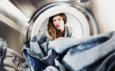 Woman looking into a washing machine, appearing concerned with denim clothes inside.