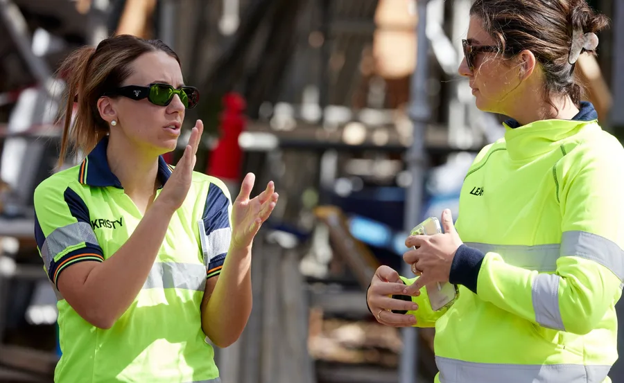 Two women in high-visibility shirts, engaged in conversation on a construction site.
