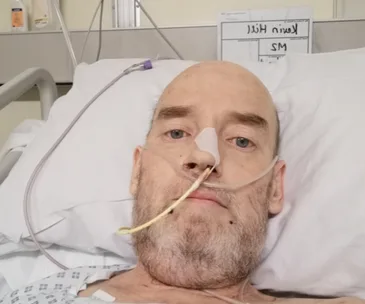 Man lying in a hospital bed with a nasal cannula and a feeding tube, looking towards the camera.
